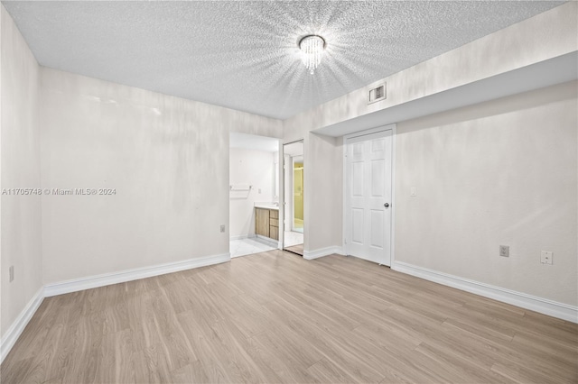 unfurnished room with an inviting chandelier, a textured ceiling, and light wood-type flooring