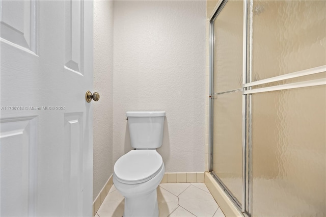 bathroom with tile patterned flooring, a shower with shower door, and toilet