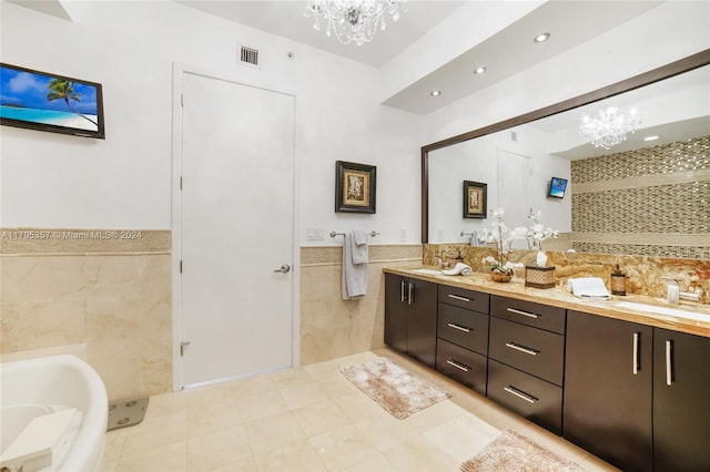 bathroom with an inviting chandelier, tile patterned flooring, a bathtub, vanity, and tile walls