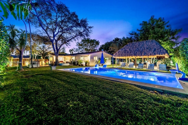 pool at dusk with a gazebo, outdoor lounge area, and a lawn