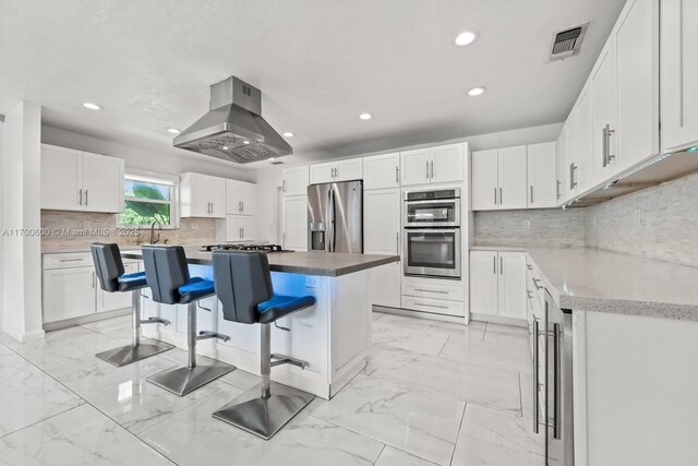 kitchen with appliances with stainless steel finishes, tasteful backsplash, ventilation hood, white cabinets, and a kitchen island