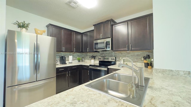 kitchen with sink, backsplash, a textured ceiling, dark brown cabinets, and appliances with stainless steel finishes