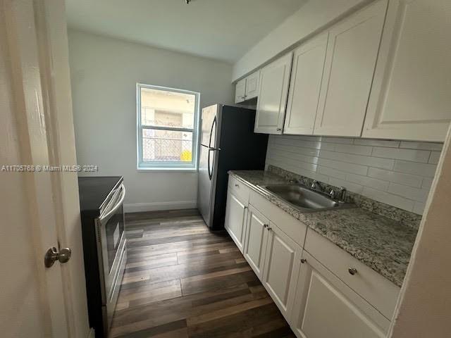 kitchen with light stone countertops, dark wood-type flooring, tasteful backsplash, white cabinets, and appliances with stainless steel finishes