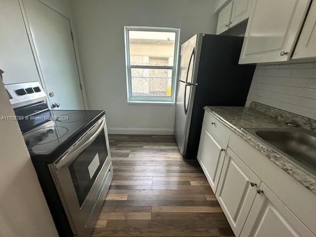 kitchen featuring light stone countertops, dark wood-type flooring, stainless steel appliances, tasteful backsplash, and white cabinets