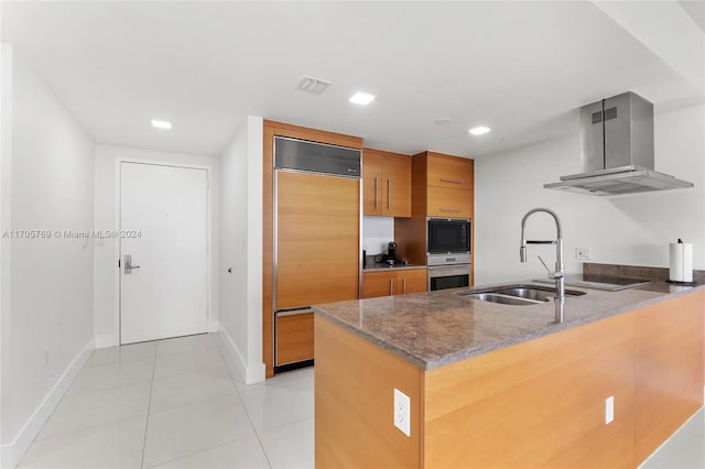 kitchen featuring kitchen peninsula, sink, wall chimney range hood, built in appliances, and light tile patterned flooring