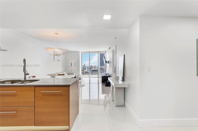 kitchen featuring sink, light tile patterned floors, pendant lighting, and a wall of windows