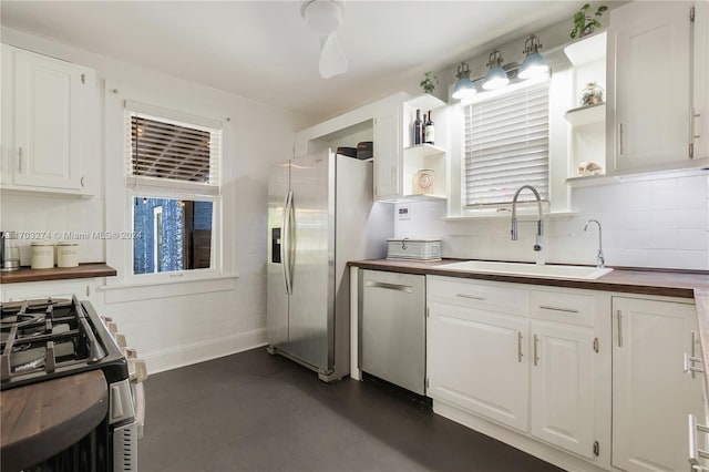 kitchen with appliances with stainless steel finishes, a healthy amount of sunlight, sink, white cabinetry, and butcher block counters