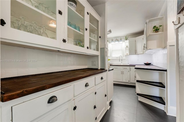 kitchen with wood counters, backsplash, dark tile patterned floors, sink, and white cabinetry