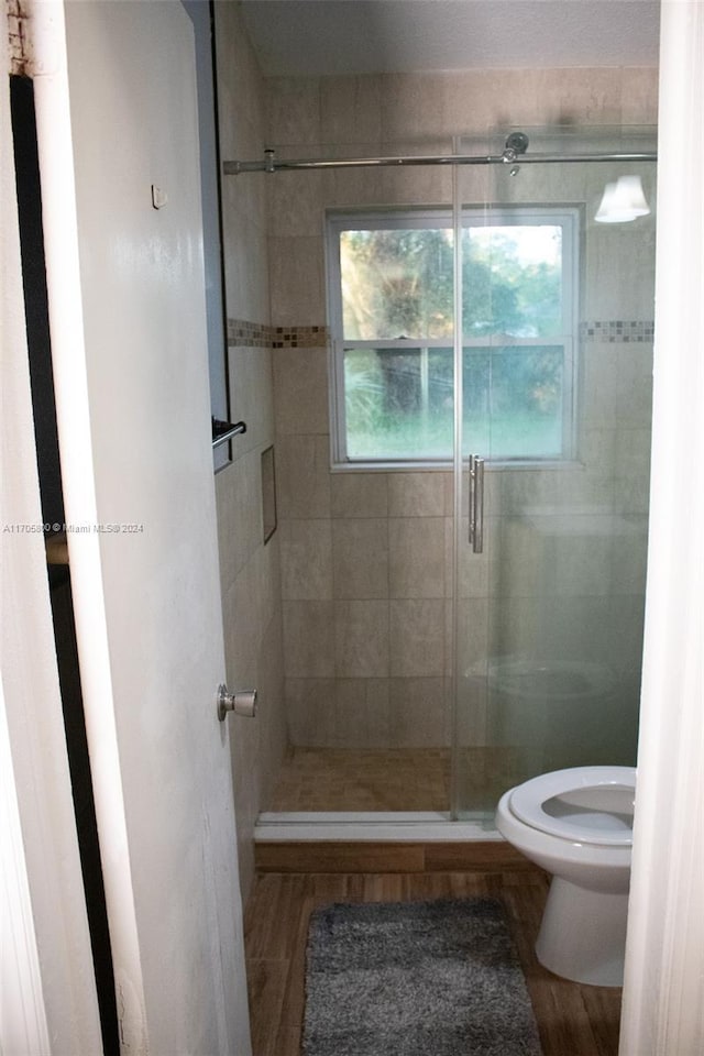 bathroom with hardwood / wood-style flooring, toilet, and a shower with shower door