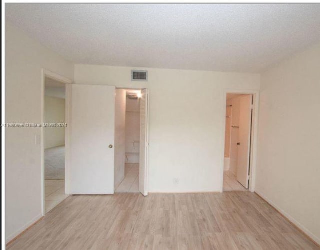 unfurnished bedroom featuring connected bathroom, a spacious closet, light hardwood / wood-style flooring, and a closet