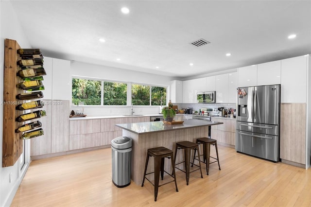 kitchen featuring white cabinetry, a center island, light hardwood / wood-style flooring, a kitchen bar, and appliances with stainless steel finishes