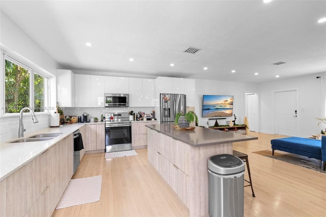 kitchen featuring light wood-type flooring, stainless steel appliances, white cabinets, a center island, and a breakfast bar area