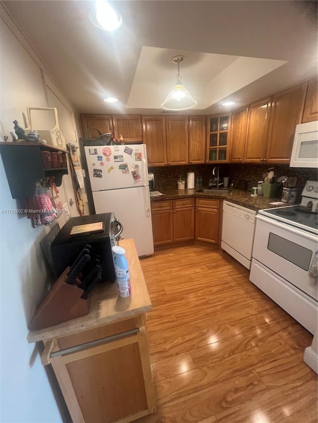 kitchen featuring sink, light wood-type flooring, a raised ceiling, pendant lighting, and white appliances