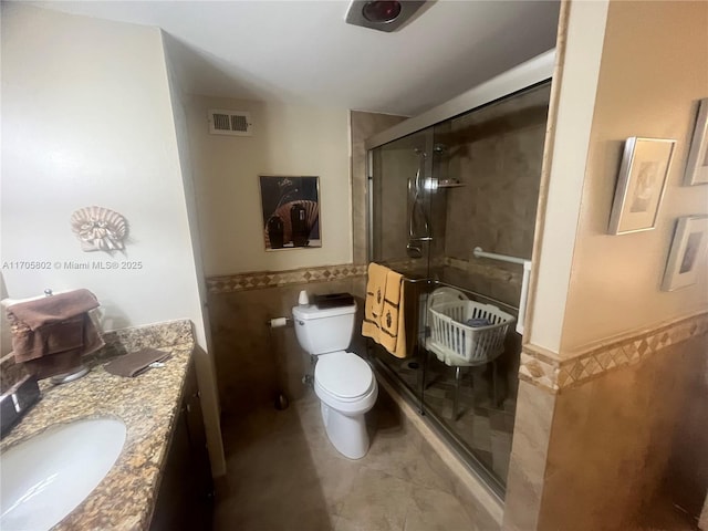 bathroom featuring tile patterned floors, toilet, a shower with shower door, tile walls, and vanity