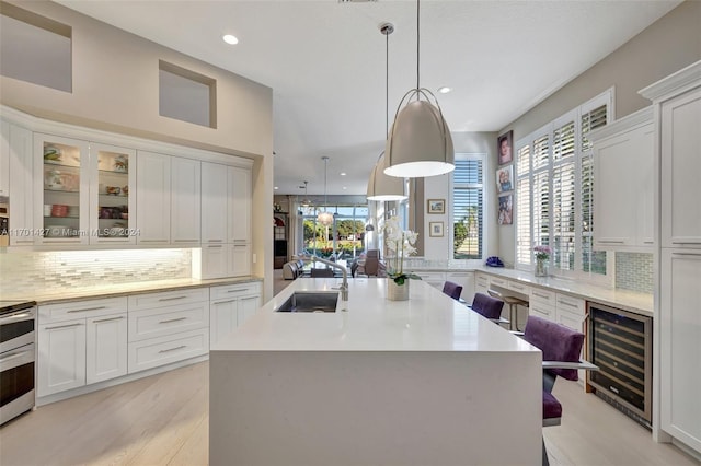 kitchen with sink, hanging light fixtures, wine cooler, an island with sink, and a breakfast bar area