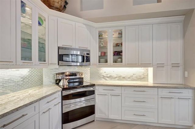 kitchen with white cabinets, decorative backsplash, light stone counters, and stainless steel appliances