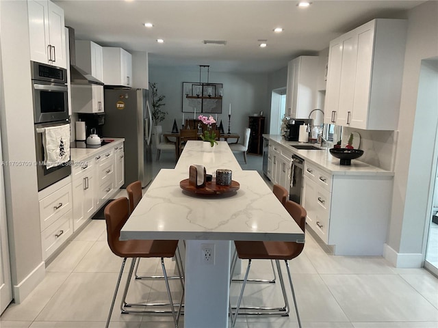 kitchen featuring a kitchen breakfast bar, sink, light stone countertops, a kitchen island, and white cabinetry