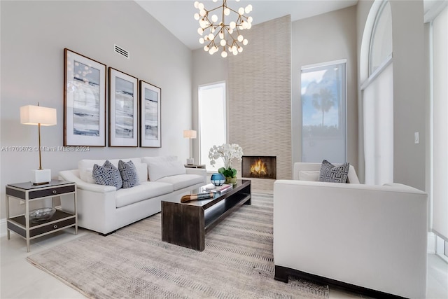 living room with a large fireplace, plenty of natural light, a towering ceiling, and a chandelier