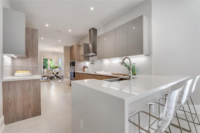 kitchen with sink, wall chimney exhaust hood, decorative light fixtures, a kitchen bar, and kitchen peninsula