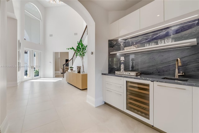 bar featuring sink, light tile patterned floors, tasteful backsplash, white cabinetry, and beverage cooler