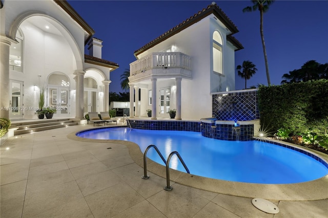 pool at twilight with a jacuzzi, pool water feature, and a patio