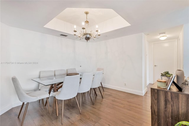 dining area with an inviting chandelier, light wood-type flooring, and a tray ceiling