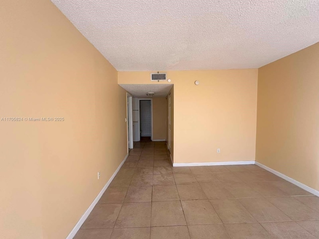 spare room with a textured ceiling, light tile patterned flooring, baseboards, and visible vents