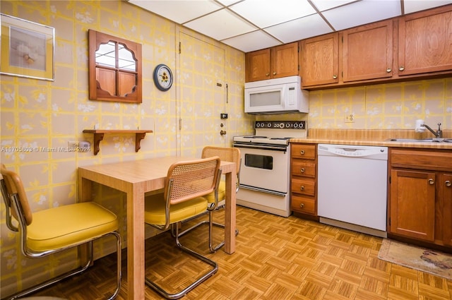 kitchen with white appliances, light parquet floors, a drop ceiling, and sink