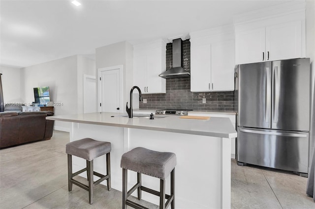 kitchen with sink, wall chimney range hood, a kitchen island with sink, white cabinets, and appliances with stainless steel finishes