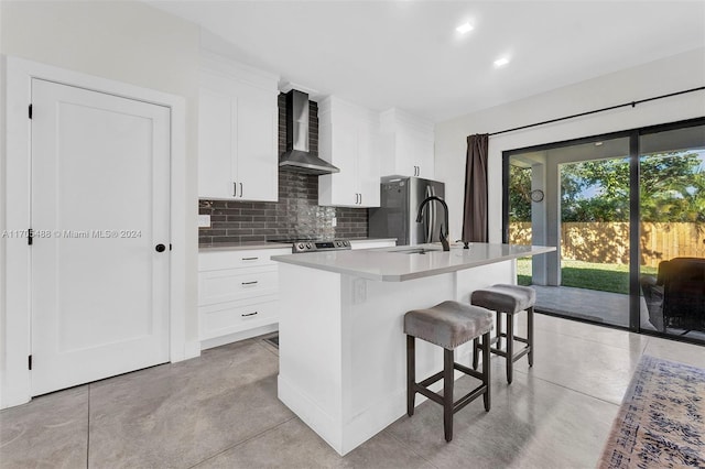 kitchen with a center island with sink, wall chimney exhaust hood, a kitchen breakfast bar, and white cabinets