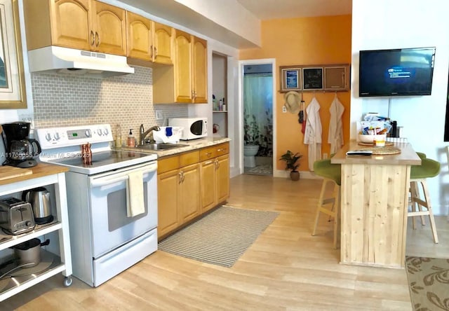 kitchen with white appliances, a breakfast bar area, light hardwood / wood-style floors, decorative backsplash, and sink