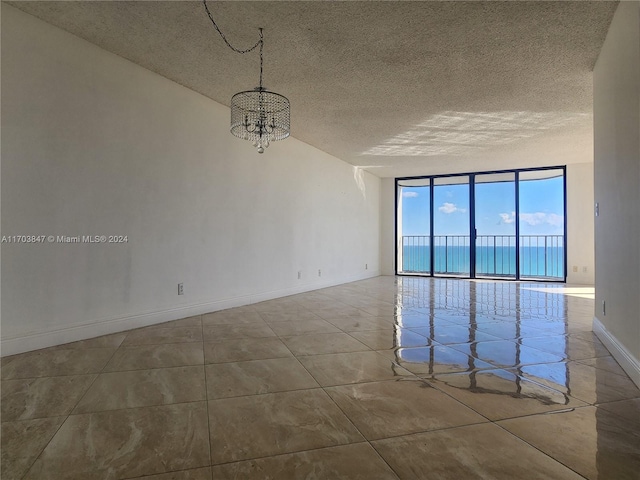 tiled empty room featuring a water view, a chandelier, a textured ceiling, and a wall of windows