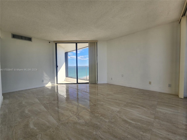 unfurnished room featuring expansive windows, a water view, and a textured ceiling