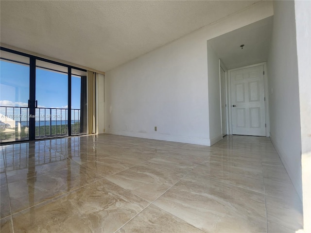 unfurnished room featuring a water view, a wall of windows, and a textured ceiling