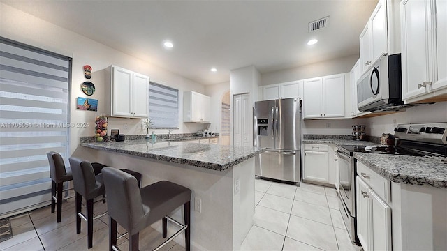 kitchen with a kitchen bar, stainless steel appliances, white cabinetry, and stone counters