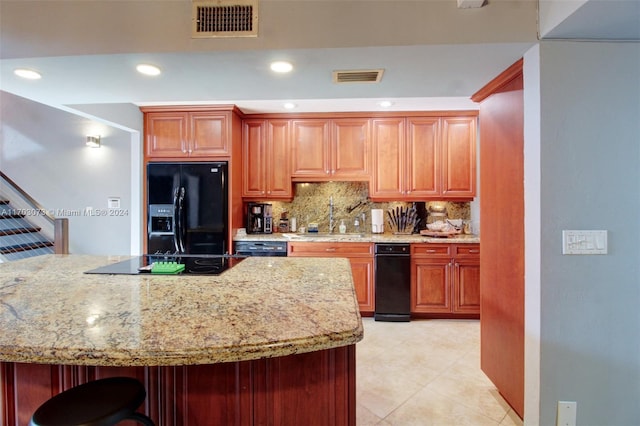 kitchen with light stone countertops, sink, a kitchen breakfast bar, tasteful backsplash, and black appliances