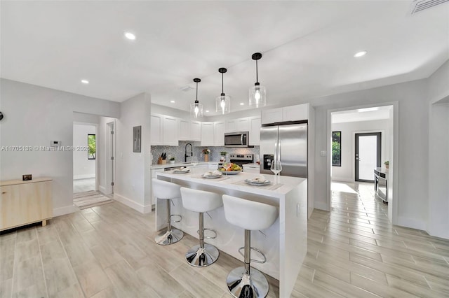 kitchen featuring appliances with stainless steel finishes, a center island, decorative backsplash, white cabinets, and decorative light fixtures