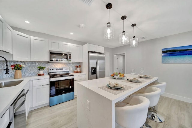 kitchen with sink, appliances with stainless steel finishes, white cabinets, pendant lighting, and backsplash