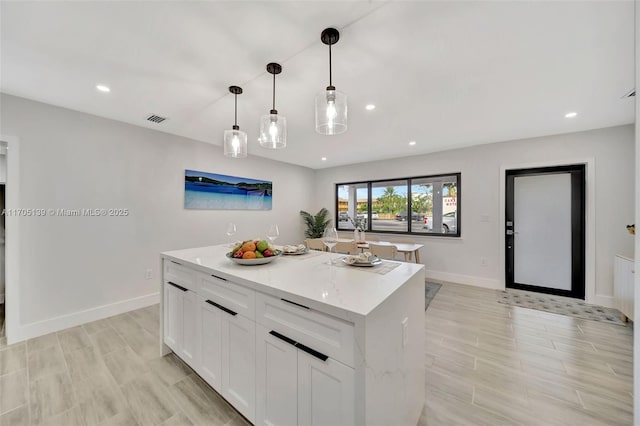 kitchen featuring a kitchen island, white cabinets, hanging light fixtures, light stone counters, and light hardwood / wood-style flooring