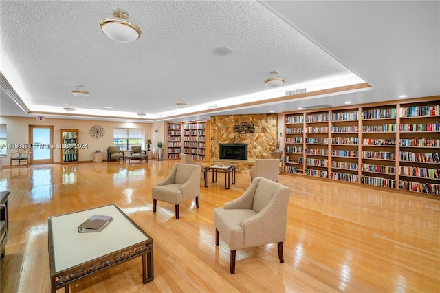 living room featuring a raised ceiling, a fireplace, light hardwood / wood-style flooring, and a textured ceiling