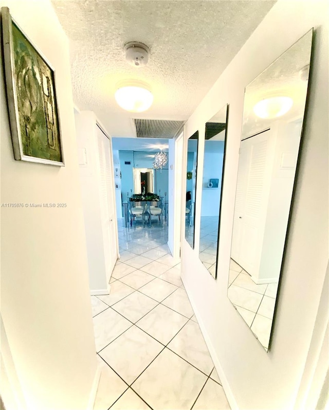 hall featuring light tile patterned floors, visible vents, baseboards, and a textured ceiling