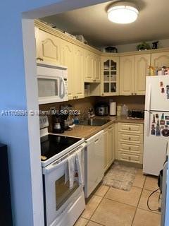 kitchen with white appliances, sink, light tile patterned floors, and cream cabinets