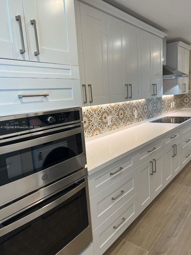 kitchen with black electric stovetop, white cabinetry, double oven, and light hardwood / wood-style flooring