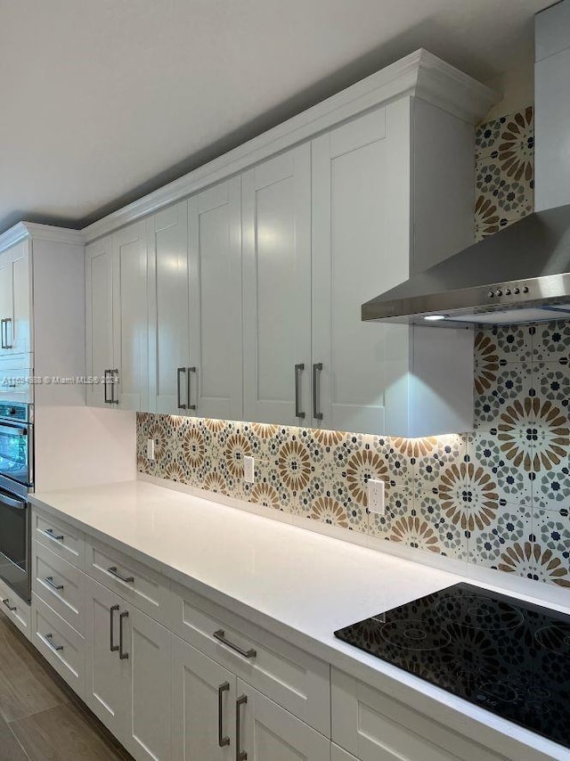 kitchen with backsplash, white cabinets, black cooktop, and wall chimney exhaust hood