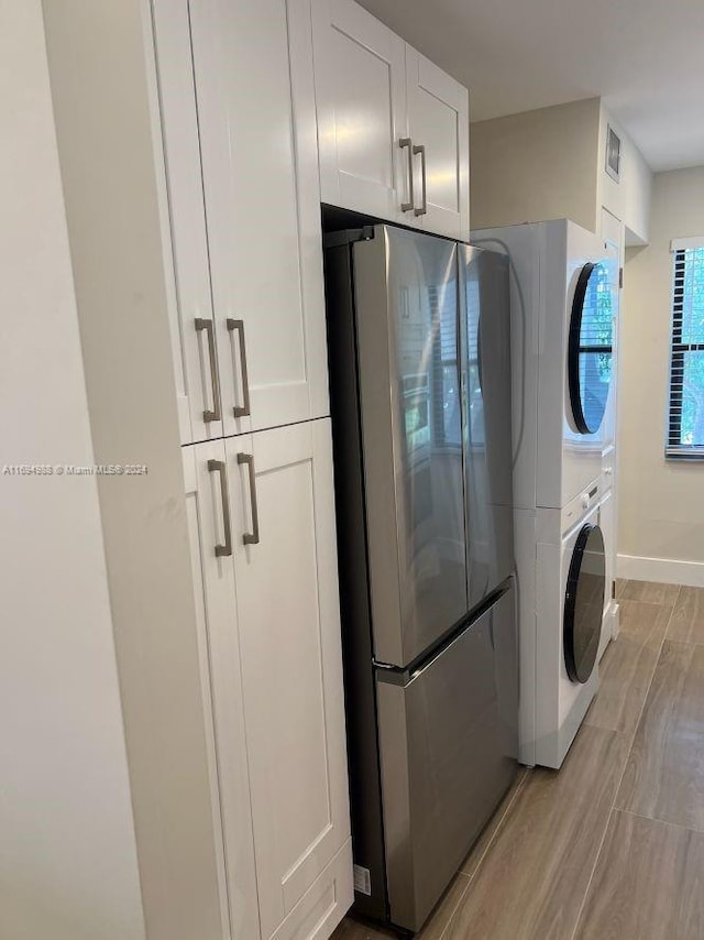 clothes washing area with cabinets, stacked washing maching and dryer, and light hardwood / wood-style flooring