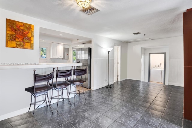 kitchen with white cabinets, stainless steel refrigerator with ice dispenser, a textured ceiling, a kitchen bar, and kitchen peninsula