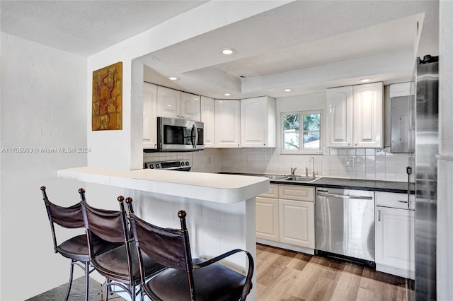 kitchen with kitchen peninsula, a kitchen bar, stainless steel appliances, sink, and white cabinetry