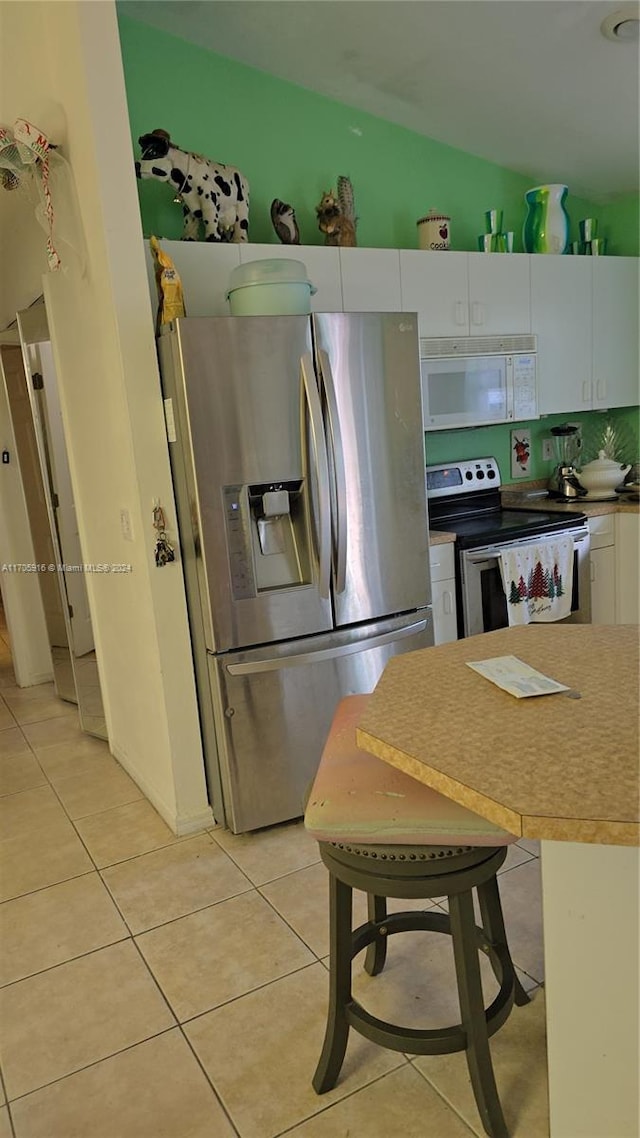 kitchen featuring white cabinets, vaulted ceiling, light tile patterned floors, a kitchen bar, and stainless steel appliances