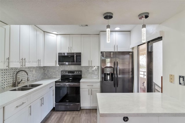 kitchen featuring stainless steel appliances, decorative backsplash, sink, white cabinetry, and decorative light fixtures