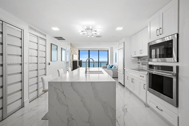 kitchen featuring built in appliances, white cabinetry, a water view, and an island with sink